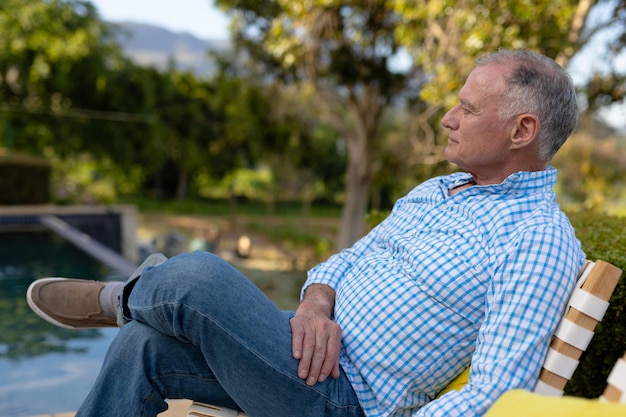 Week-end à la maison. Vue latérale d'un homme de race blanche senior dans le jardin, assis sur une chaise se détendre et penser