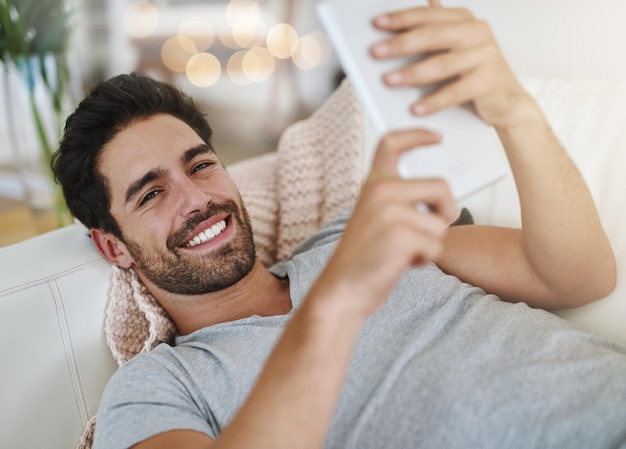 Week-end paresseux en ligne Photo d'un jeune homme naviguant sur Internet à la maison sur une tablette numérique