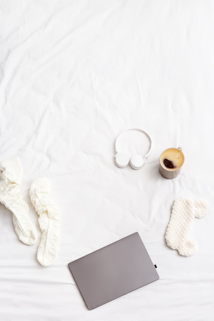 Week-end paresseux Matin, à plat avec ordinateur portable, chaussettes chaudes, tasse de café, écouteurs sans fil, masque pour dormir sur le lit