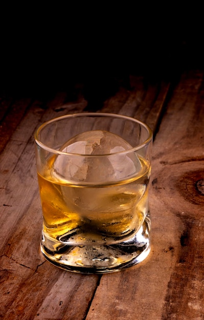Whiskey single malt dans un verre spécifique avec de la glace transparente dans une sphère isolée sur une table en bois rustique à fond sombre