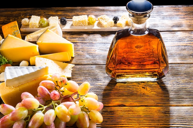 Whisky ou brandy dans une carafe moderne et élégante sur une table de buffet avec un assortiment de fromages sur un plateau et une grappe de raisins frais