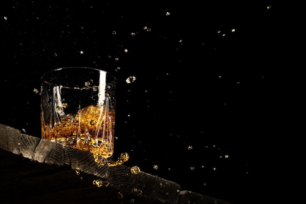 Whisky dans un verre sur fond noir sur une table en bois.