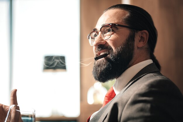 Photo whisky et fumer. homme d'affaires prospère vêtu d'un costume gris foncé, boire du whisky et fumer