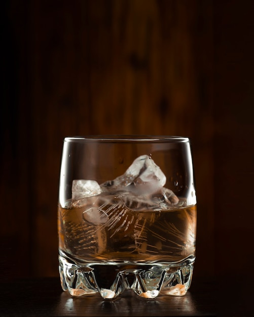 Whisky avec de la glace sur un fond en bois foncé.