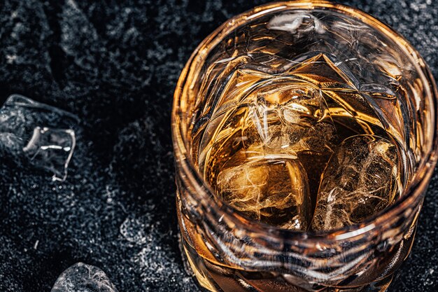 Whisky avec de la glace sur un fond sombre en pierre.