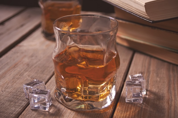 Whisky avec de la glace sur une table en bois. Livres anciens à proximité.