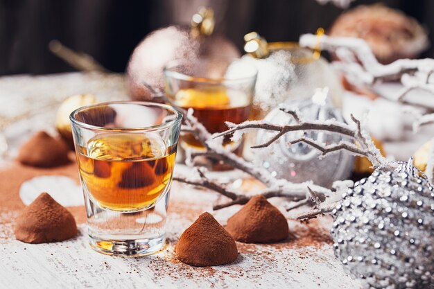 Whisky ou liqueur, bonbons au chocolat aux truffes en poudre de cacao et décorations de Noël sur fond de bois blanc.