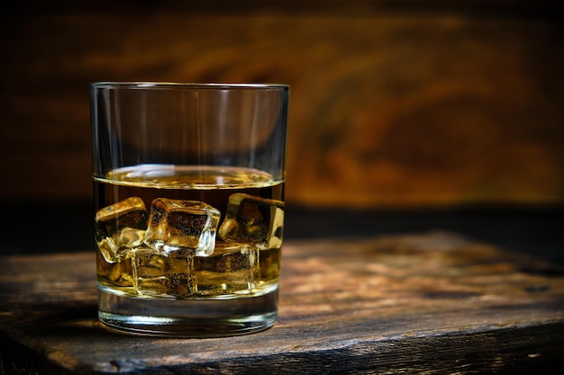 Whisky réfrigéré en verre avec des glaçons sur fond de bois dans la cave.