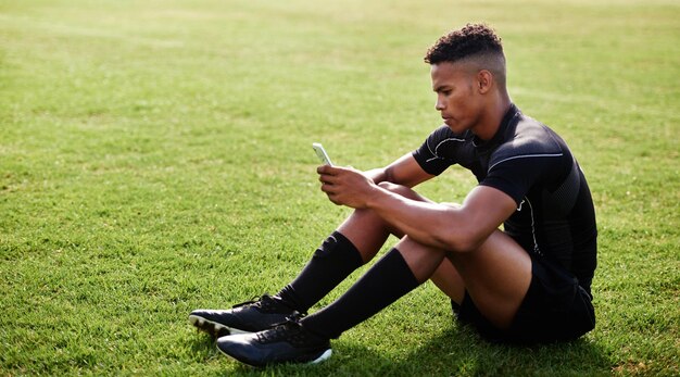 Le wifi est aussi chaud que ses compétences Photo d'un jeune homme assis sur le terrain et utilisant un smartphone lors d'un match de rugby