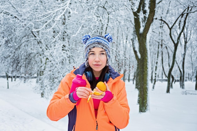 Winter run carburant femme fitness sportive dans les écouteurs mangeant de la mandarine et de l'eau potable à l'extérieur dans