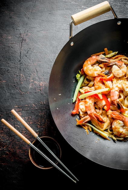 Wok chinois nouilles Udon dans une poêle wok avec des baguettes et de la sauce soja