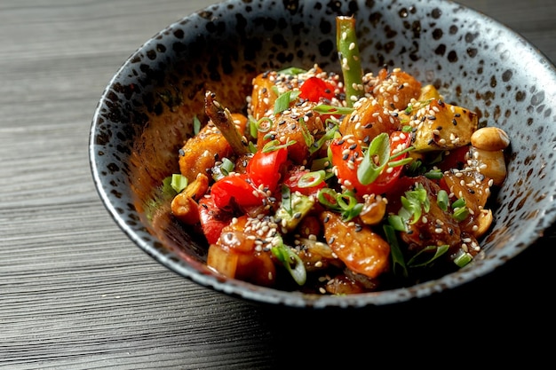 Wok de poulet à la sauce aigre-douce avec des légumes dans une assiette noire sur fond sombre