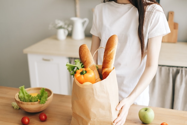 Woman hold eco shopping bag avec des légumes frais et de la baguette dans la cuisine moderne
