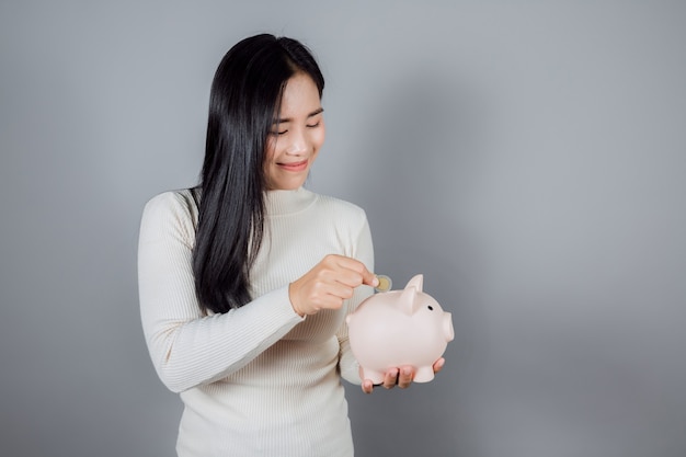 Woman Putting Coin In Piggy Bank sur fond gris
