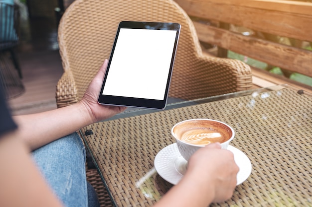 Woman's hands holding black tablet pc avec écran vide tout en buvant du café dans un café moderne