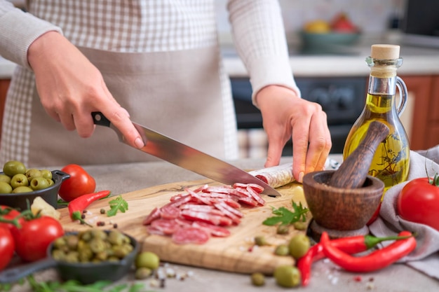 Woman slicing saucisse espagnole fuet salami avec couteau sur une cuisine domestique