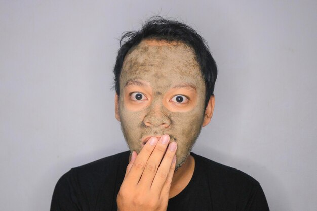 Photo wow asian man a été choqué et regarde la caméra quand il utilise un masque de beauté