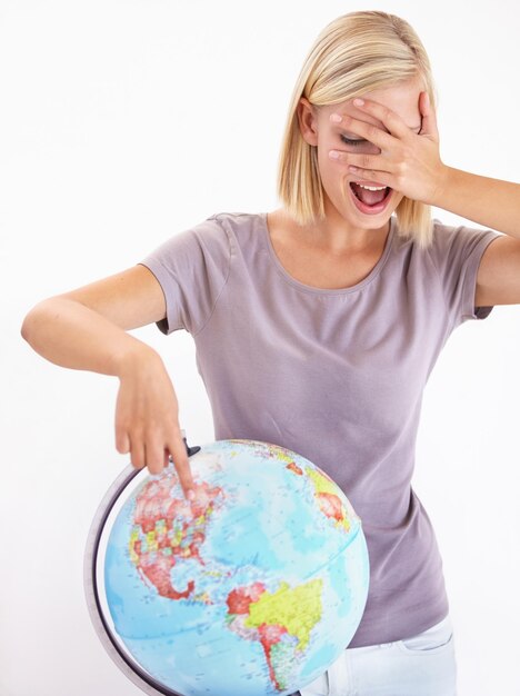 Photo wow deviner ou pointer et une femme avec un globe dans le studio sur un fond blanc pour le choix de la destination planète du monde et le geste de la main à un emplacement sur la terre pour la décision de voyage à l'étranger ou la sélection