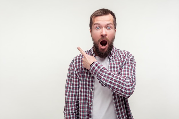 Wow, regarde là. Portrait d'un homme barbu choqué en chemise à carreaux décontractée pointant le doigt vers le haut, espace vide pour la publicité, l'air surpris étonné. tourné en studio isolé sur fond blanc