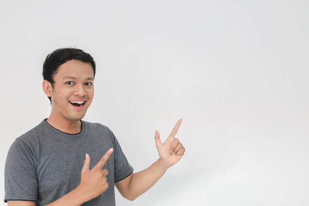 Wow et visage surpris avec le sourire du jeune homme asiatique en t-shirt gris avec point de main sur l'espace vide