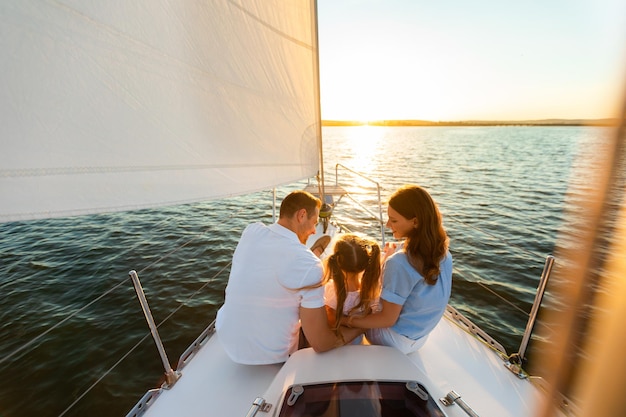 Yacht de famille à voile. Parents et petite fille assis ensemble sur le pont du voilier étreignant profitant d'un voyage en mer. Vue arrière, espace libre