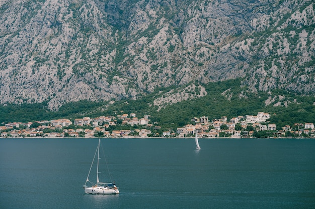 Yacht à voile blanc navigue sur la baie de Kotor dans le contexte de la ville dans les montagnes