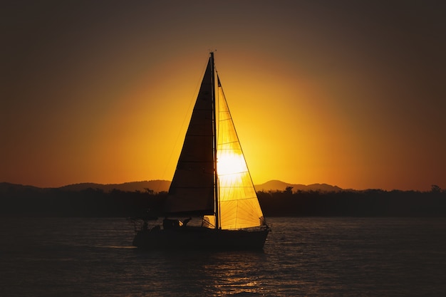 Yacht à voile contre le coucher du soleil