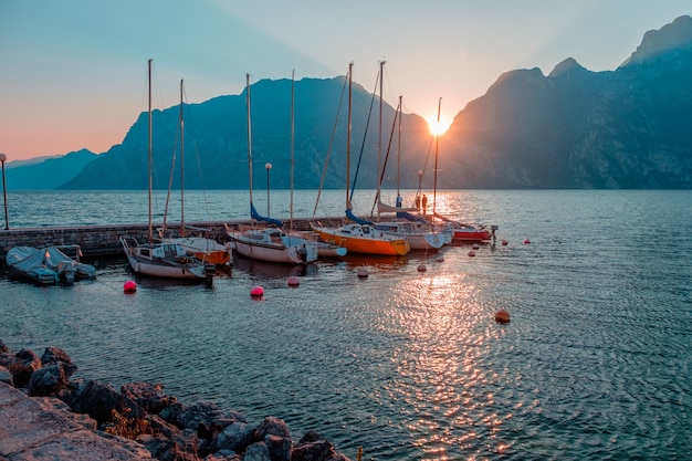 Yachts à l'embarcadère pendant le coucher du soleil sur le lac de Garde. Coucher de soleil sur la riva del garda. Le soleil se couche dans les montagnes. Lac au nord de l'Italie.