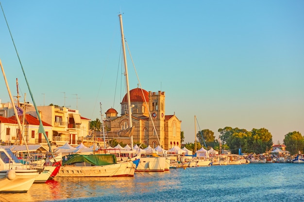 Yachts et front de mer avec l'église Ekklisia Isodia Theotokou au coucher du soleil dans la ville d'Egine, îles Saroniques, Grèce