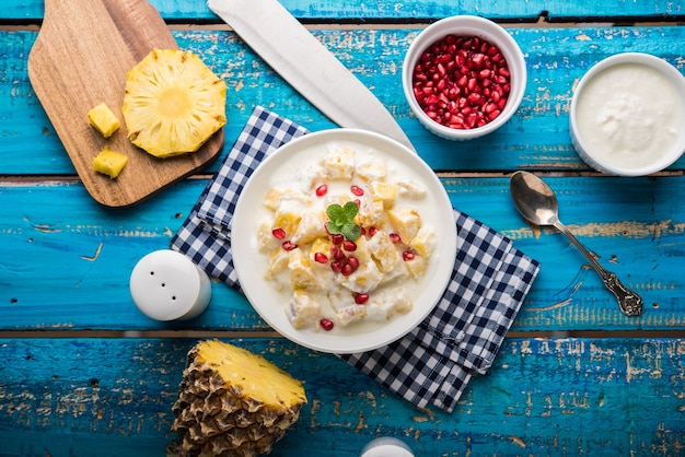 Yaourt & Ananas ou Ananas Raita, servis dans un bol et garnis de menthe et de grenade, sur fond coloré ou en bois. Mise au point sélective