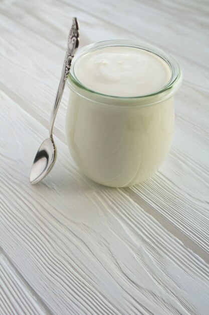 Photo yaourt au lait naturel dans le bocal en verre sur le bois blanc