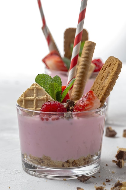 Yaourt fait maison aux fruits rouges, framboises, myrtilles, mûres et fraises, biscuits et chocolat sur une table en bois blanche. Concept d'aliments sains