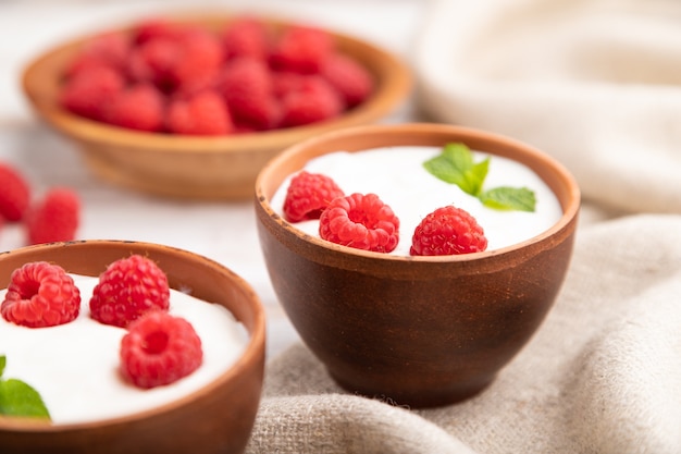 Yaourt à la framboise dans des tasses d'argile sur une surface en bois blanc et textile en lin