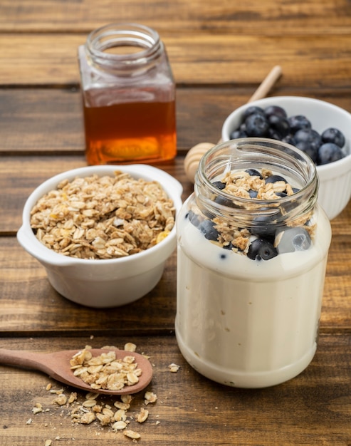 Yaourt, granola, myrtille et miel sur table en bois.