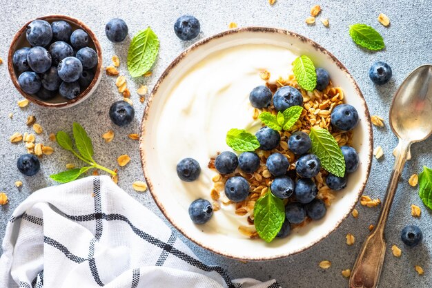 Yaourt avec granola et myrtilles fraîches sur une table en pierre claire Petit-déjeuner sain Vue de dessus