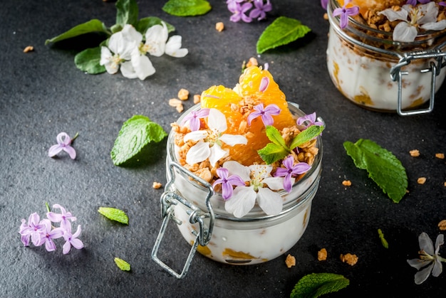 Yaourt avec granola, orange, menthe et fleurs comestibles
