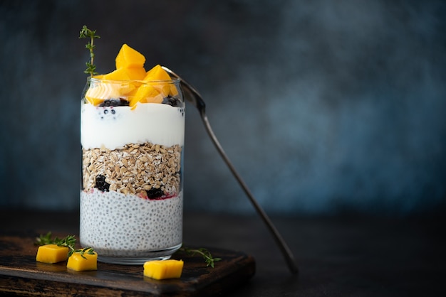 Yaourt grec avec flocons d'avoine, graines de chia et mangue sur un bocal en verre