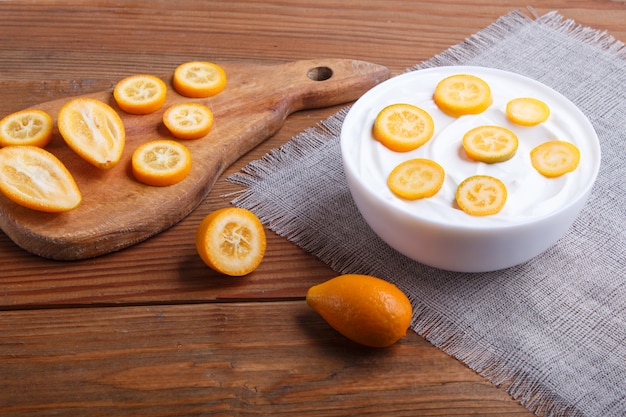 Yaourt grec avec des morceaux de kumquat dans une assiette blanche sur un fond en bois marron