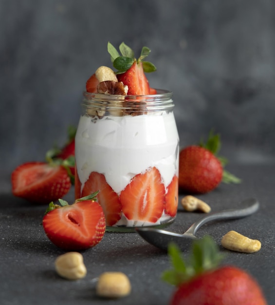 Yaourt grec noix et fraises dans un bocal en verre sur une table grise avec une cuillère en gros plan