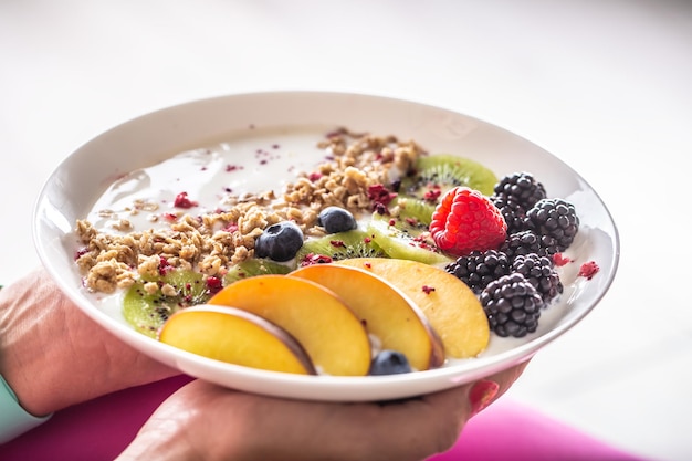 Yaourt mûre muesli framboises myrtilles kiwi et pêches dans un bol blanc