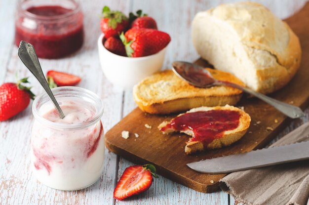 Yaourt nature, fraises fraîches, confiture de fraises et pain, sur fond de bois.