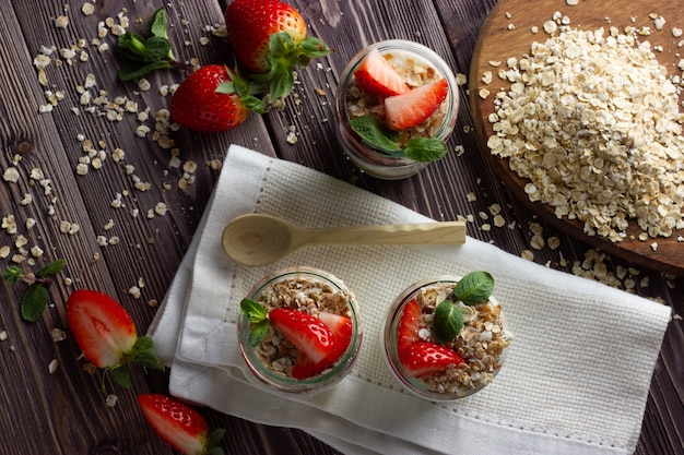 Yaourt nature en petit pot avec confiture, muesli et fraise fraîche, feuilles de menthe. Concept de petit-déjeuner sain.