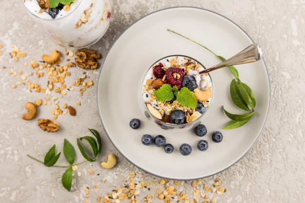 Yaourt naturel avec granola et baies dans un bécher en verre sur une plaque en céramique et un fond en béton. petit déjeuner léger, nourriture saine.