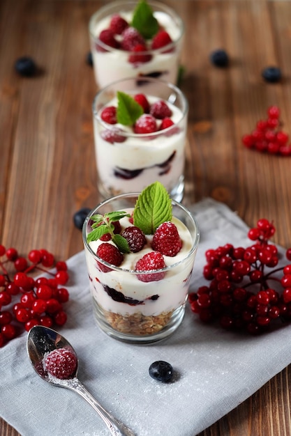 Yaourt petit-déjeuner sain avec des baies fraîches et du muesli servi dans un bocal en verre sur fond de bois