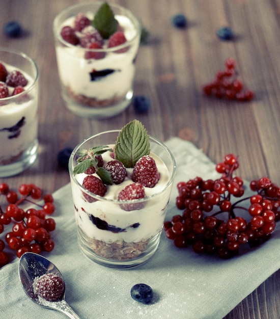 Yaourt petit-déjeuner sain avec des baies fraîches et du muesli servi dans un bocal en verre sur fond de bois