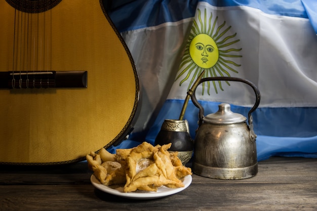 Photo yerba mate, guitare et pâtisseries frites avec drapeau argentin à l'arrière