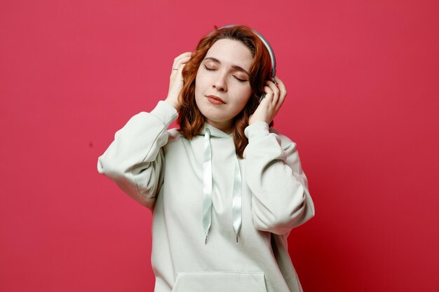 Avec les yeux fermés jeune belle fille en chandail blanc portant des écouteurs isolés sur fond rose