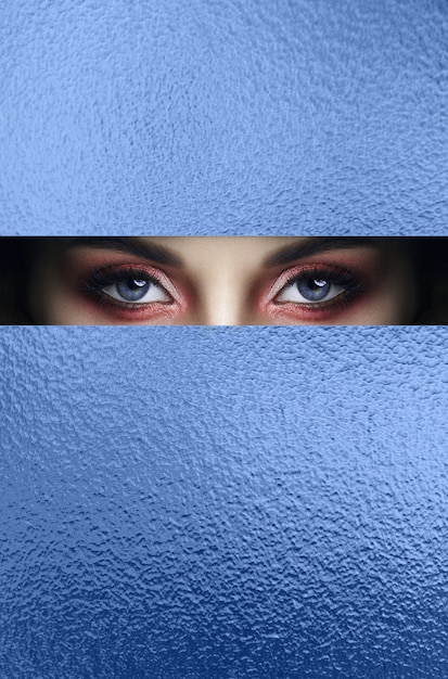 yeux de maquillage rouge d'une jeune fille dans un trou de papier bleu