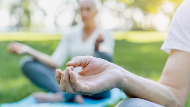 Yoga au parc Gros plan d'un couple âgé assis en posture de lotus sur l'herbe verte en méditation
