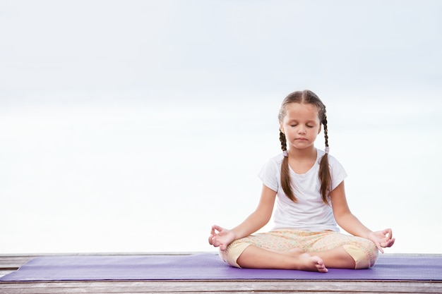 Photo yoga enfant méditant sur une plate-forme en bois